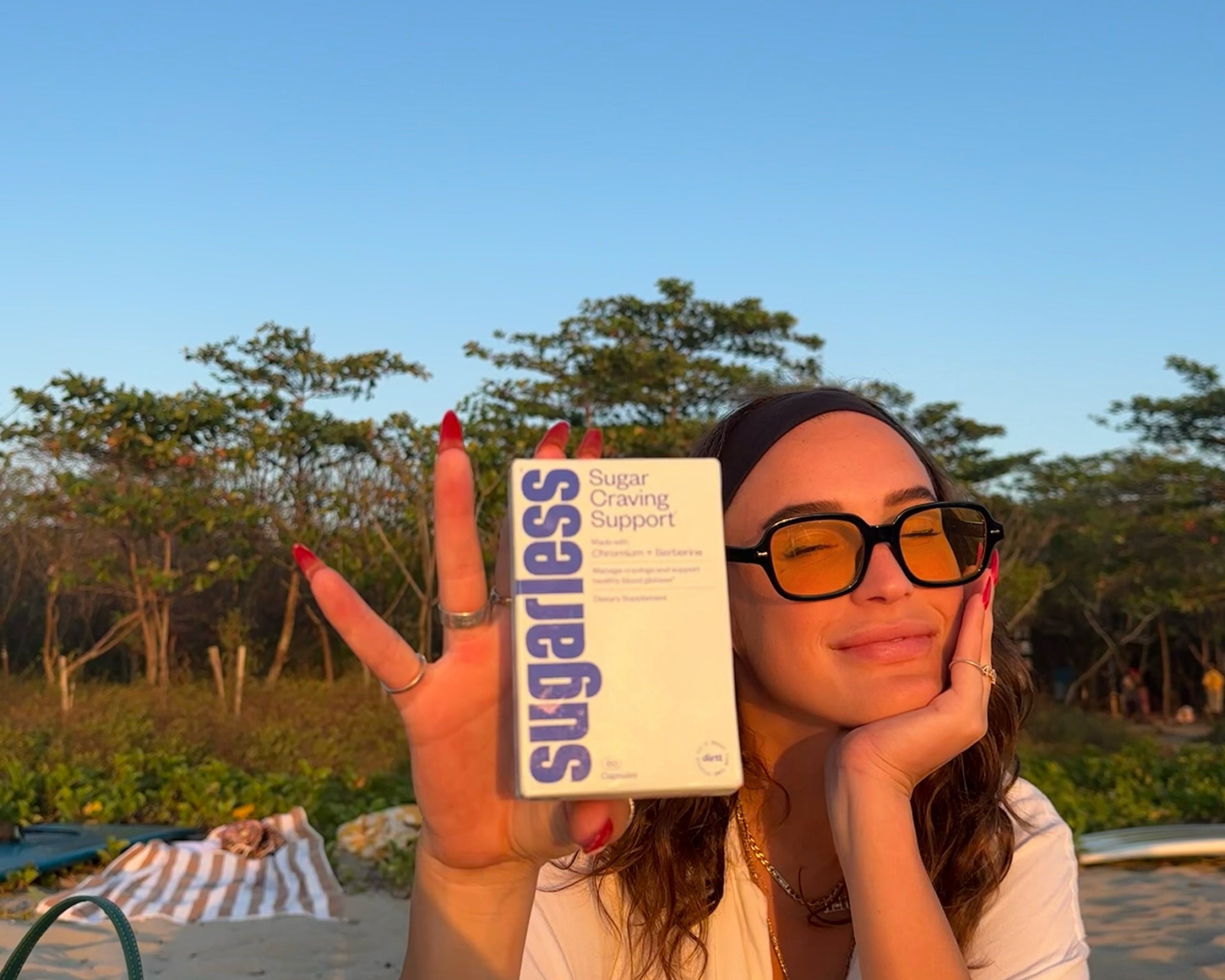 a woman holding a box Sugarless Sugar Craving Support supplement outside in the sunset