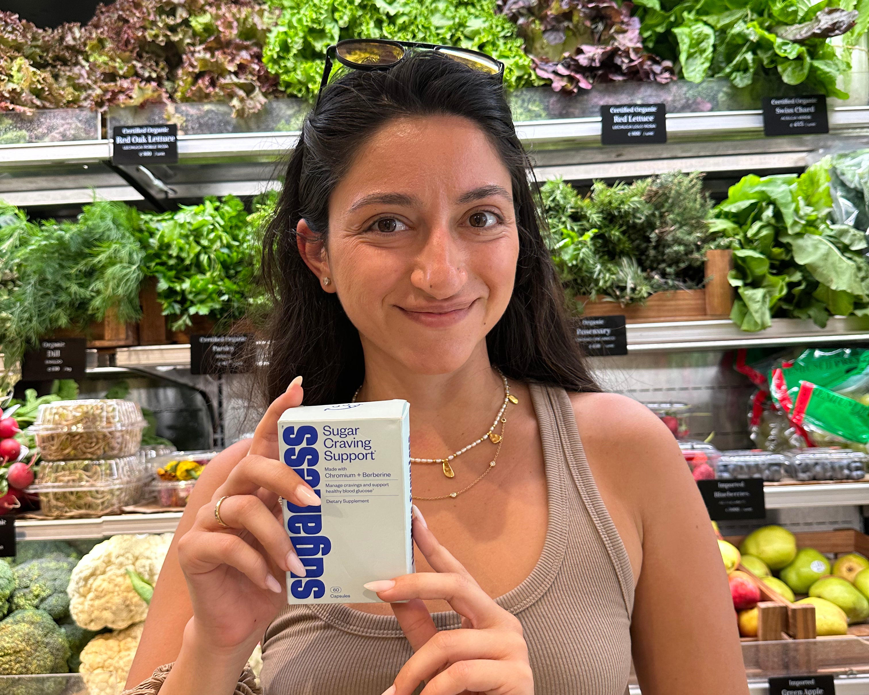 a woman holding a box Sugarless Sugar Craving Support supplement inside a grocery store